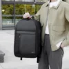 Мъж държи раница за пътуване STELS CityPro 30, поставена върху куфар, готов за пътуване.